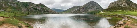 paisaje en la orilla de un aparente lago en primer plano rodeado de montaña con un cielo nublado